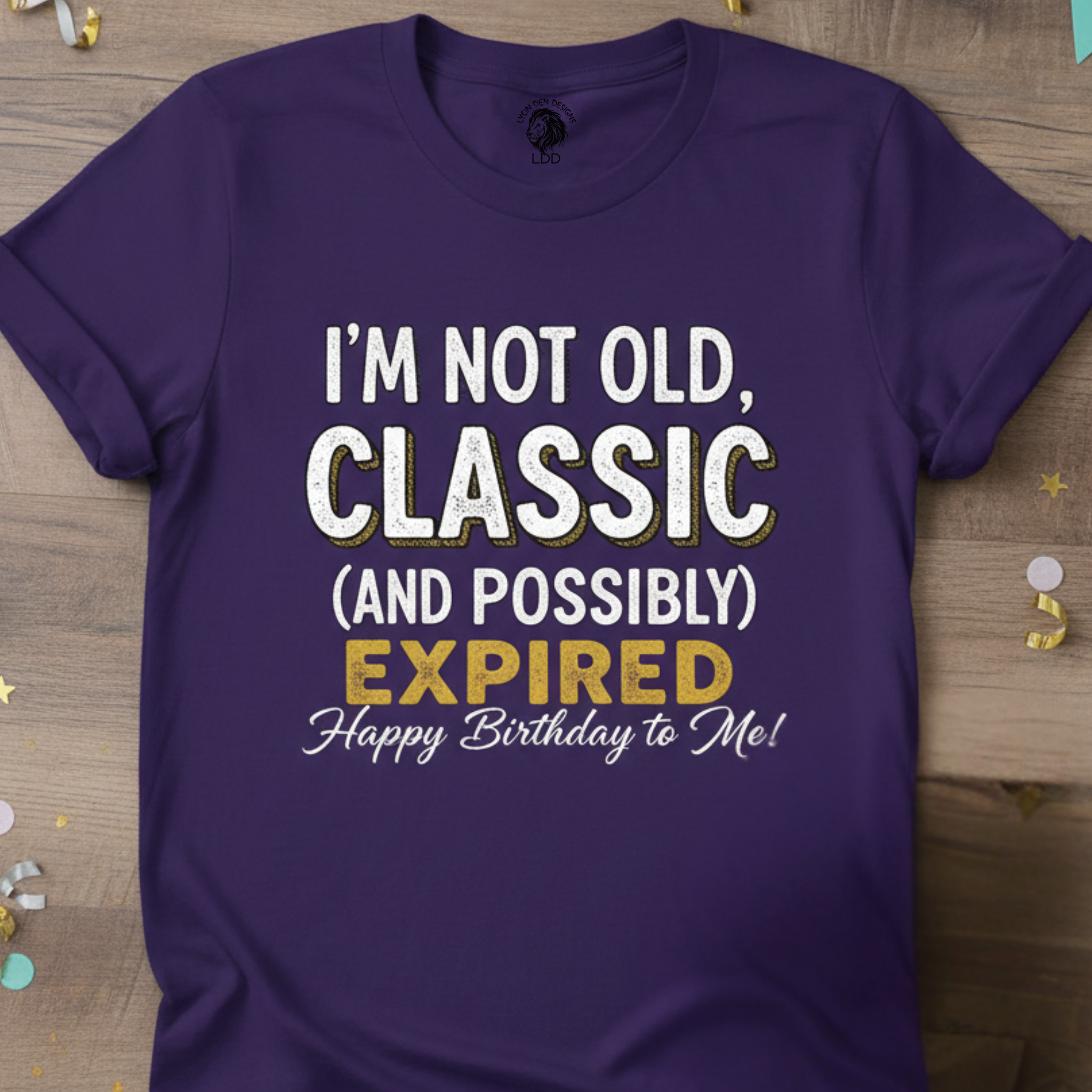 Purple t-shirt with humorous birthday message on a wooden surface